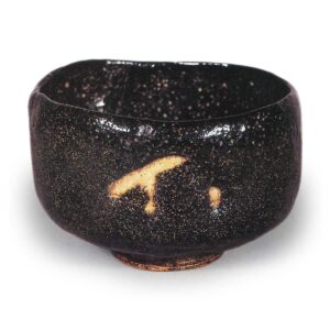 Black Tea Bowl, Inscription: “Shishi,” by Dōnyū

Height: 8.4 cm; Mouth diameter: 12.3–12.5 cm; Foot diameter: 5.2 cm
On the underside of the inner box lid, Jushinsai has inscribed: “Nonkaku Black Tea Bowl, Shishi-boku-gei, Left (Seal).” It is understood that this name was derived from the Noh play “Ishibashi” (Stone Bridge), as the white glaze pattern on the body is interpreted as resembling a bridge.
Although its form resembles that of “Chidori,” the rim is drawn inward. The piece is thin overall, with the rim being particularly thin and skillfully crafted, featuring variations in height along the rim. As is typical, the interior is wide and generous, while the footring is flat, sharply defined, and the indentation at the base of the footring is deep. A vivid “Raku” mark is stamped in the center of the foot, and while the foot and its surroundings are not covered in black glaze, they are coated with a thin, transparent glaze; three irregular marks remain on the foot’s base.
A jet-black glaze completely covers both the interior and exterior, but the glaze has flowed down to the lower edge on one side, revealing a faint white streak where the glaze breaks. This streak is caused by impurities drifting within the black glaze. Traces of the kiln shelf remain on the lower rim. While the form is gentle, this tea bowl displays techniques characteristic of Dōin throughout. One of the “Seven Varieties of Nonkō.”